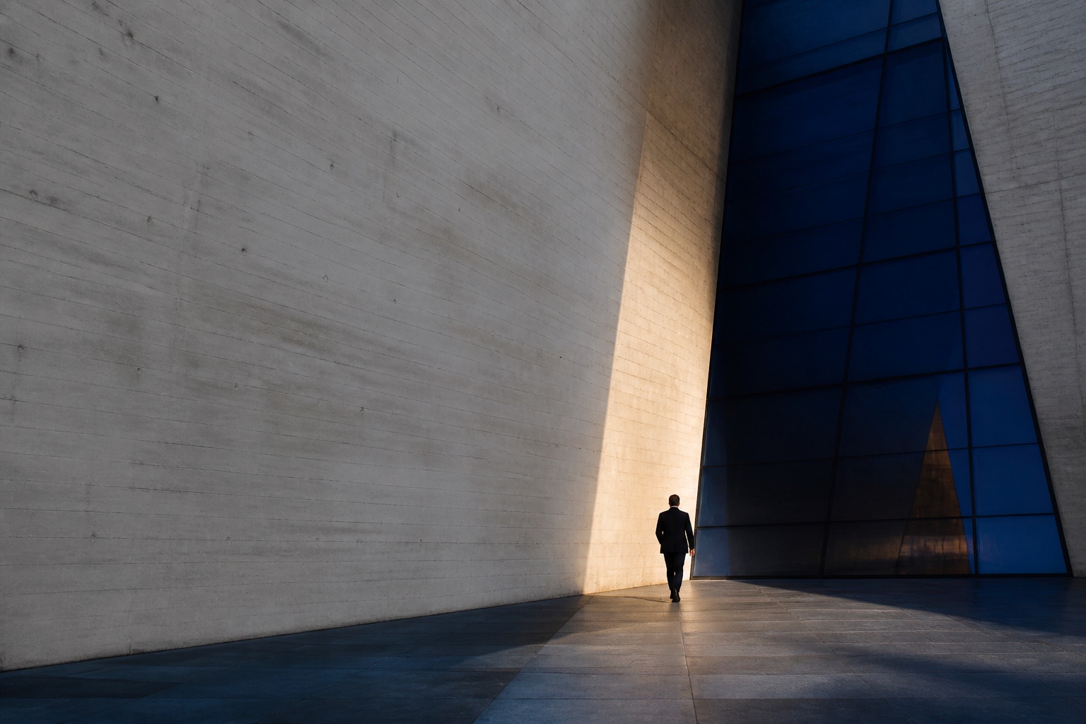 A figure moving through the intersection of concrete and blue glass architecture