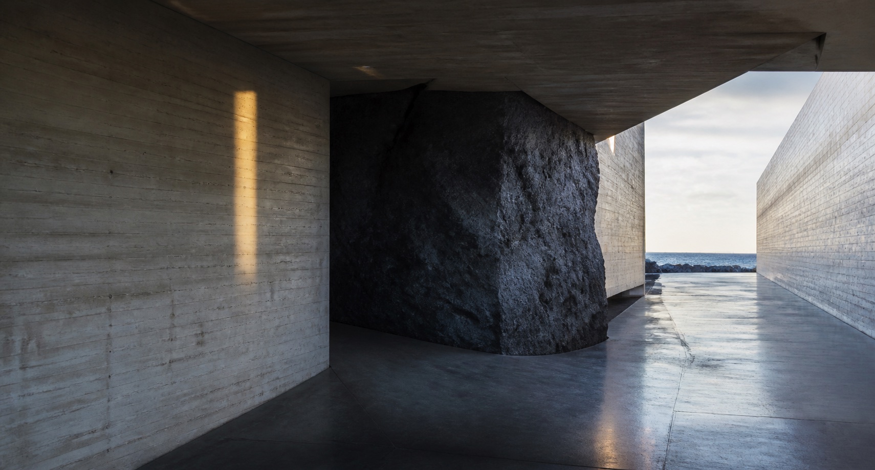 A concrete coastal passage changing direction around a dark basalt form
